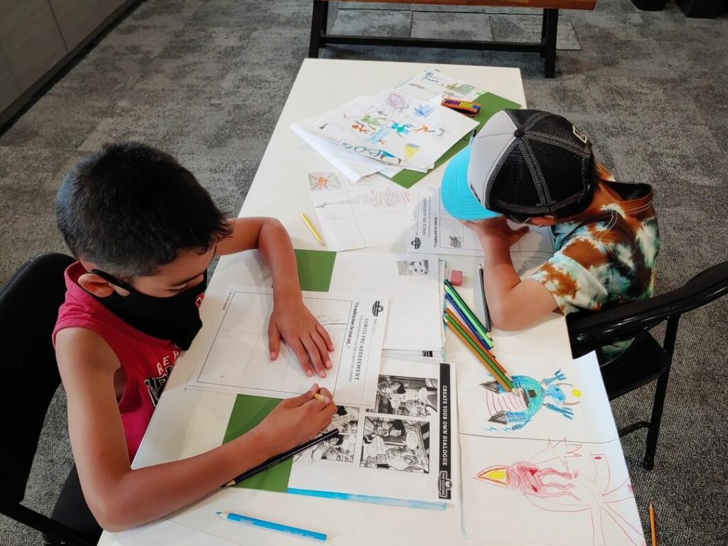 Photo of 2 children sitting at a table drawing