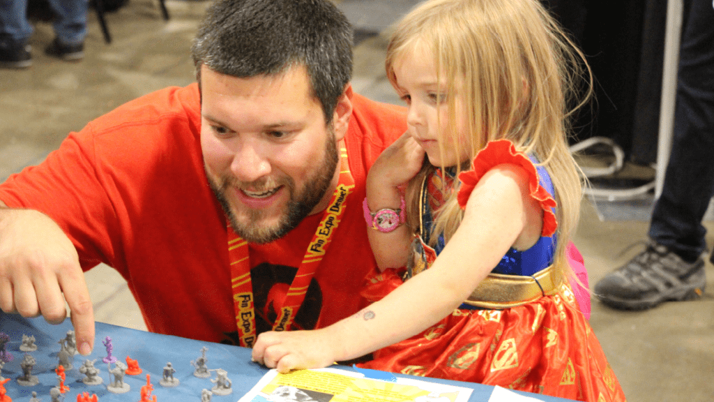 Adult and child select tabletop miniatures as prizes for completing activities in the PCC Kids' Lab at FAN EXPO Denver 
